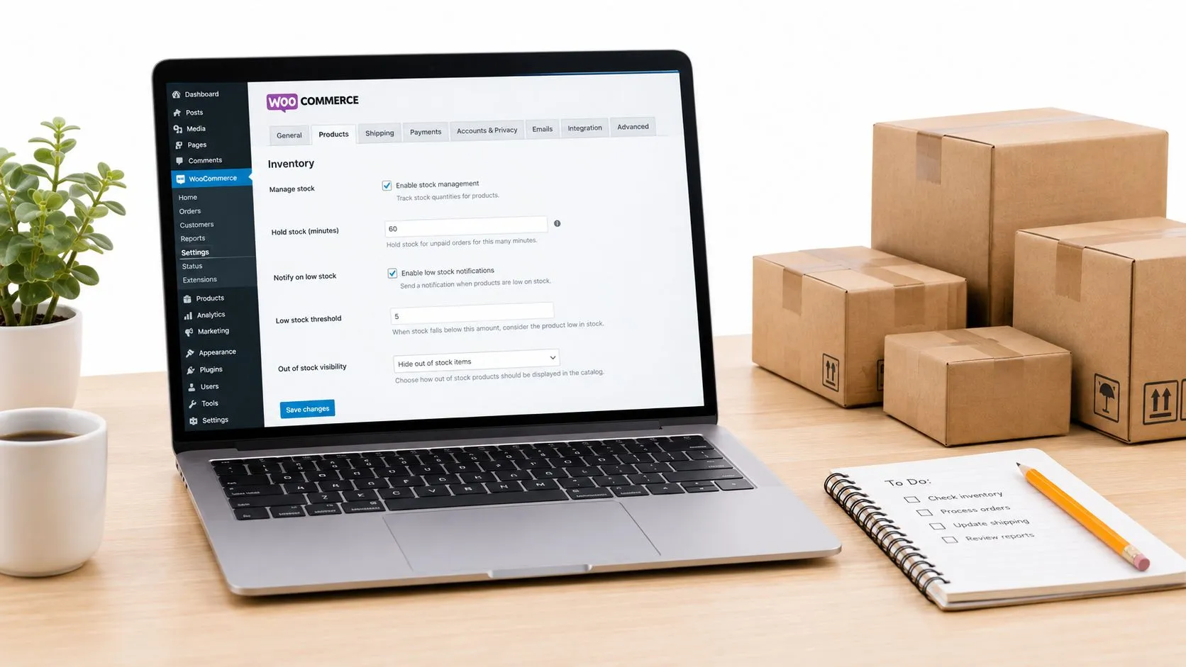 Ordinateur portable affichant les réglages d'inventaire de WooCommerce, avec la gestion du stock activée et un seuil de stock faible, à côté de cartons d'expédition